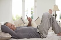 Homme âgé utilisant un téléphone portable sur le lit — Photo de stock