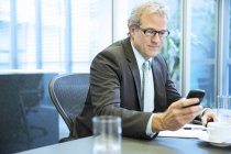 Messagerie texte homme d'affaires avec téléphone portable dans la salle de conférence au bureau moderne — Photo de stock