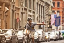 Mann fährt Fahrrad auf Stadtstraße und gestikuliert beim Abbiegen — Stockfoto