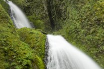 Waterfall rushing over green rocky hillside — Stock Photo