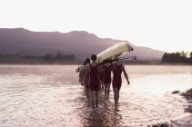 Rowing team carrying scull into lake — Stock Photo