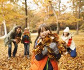 Счастливая семья играет в осенние листья — стоковое фото