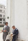 Businessmen with suitcases talking and leaning against building in Venice — Stock Photo