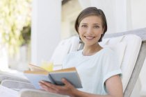 Smiling woman reading book in lawn chair — Stock Photo