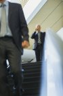 Businessman talking on cell phone at top of escalator in office — Stock Photo