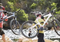 Hombres adultos caucásicos llevando bicicletas de montaña en el río - foto de stock