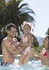 Счастливая молодая семья играет в бассейне — стоковое фото