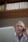 Older man talking on cell phone at desk — Stock Photo