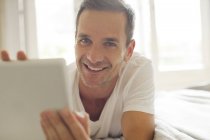 Портрет усміхненого чоловіка, який використовує цифровий планшет у ліжку — стокове фото