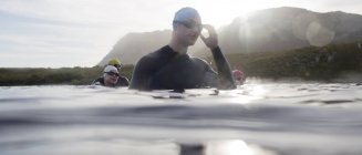 Уверенных и сильных триатлонистов в гидрокостюмах, стоящих в воде — стоковое фото