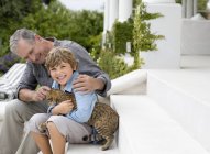 Взрослый мужчина и внук ласкают кошку на ступеньках — стоковое фото