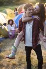 Man piggybacking woman outside tents at music festival — Stock Photo