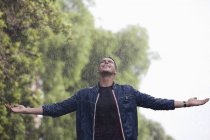 Человек с распростертыми руками под дождем — стоковое фото
