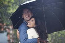 Pareja feliz abrazándose bajo el paraguas bajo la lluvia - foto de stock