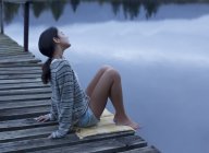 Спокойная женщина, сидящая на пристани над озером — стоковое фото