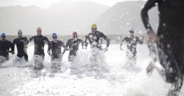 Triatletas seguros y fuertes en trajes de neopreno que corren en olas - foto de stock