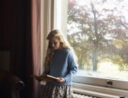 Chica leyendo por ventana - foto de stock
