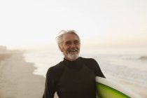Surfeur plus âgé portant la planche sur la plage — Photo de stock