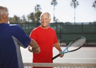 Hombres mayores estrechando la mano en la cancha de tenis - foto de stock