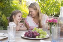 Mother and daughter smiling at table outdoors — Stock Photo