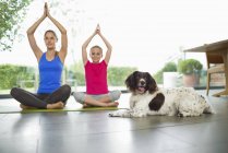 Perro sentado con madre e hija practicando yoga - foto de stock