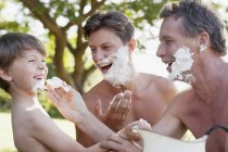 Игривые мужчины разных поколений наносят крем для бритья на лица — стоковое фото