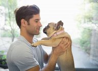 Вид збоку усміхненого чоловіка тримає собаку в приміщенні — стокове фото