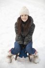 Portrait de femme souriante assise sur un traîneau dans la neige — Photo de stock