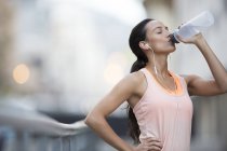 Mujer bebiendo agua después de hacer ejercicio en la calle de la ciudad - foto de stock