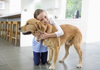 Smiling girl hugging dog in kitchen at modern home — Stock Photo