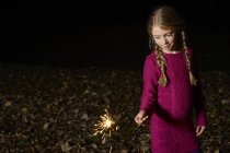 Girl playing with sparkler outdoors at night — Stock Photo