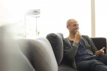 Молодой привлекательный мужчина разговаривает на гарнитуре на диване — стоковое фото