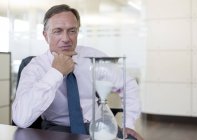 Бизнесмен смотрит песочные часы в современном офисе — стоковое фото