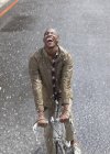 Entusiasta hombre negro montar en bicicleta en la lluvia - foto de stock