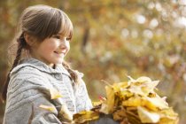 Menina sorrindo jogando em folhas de outono — Fotografia de Stock