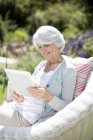 Mulher idosa usando tablet digital em poltrona — Fotografia de Stock