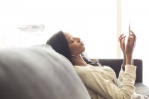Giovane donna attraente ascoltando le cuffie sul divano — Foto stock