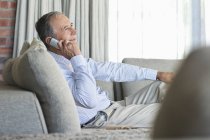 Пожилой мужчина разговаривает по мобильному телефону на диване — стоковое фото