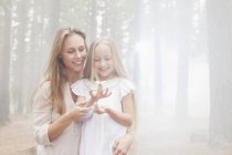 Smiling mother and daughter in sunny woods — Stock Photo