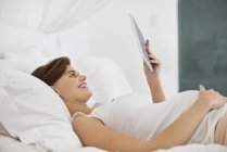 Вагітна жінка використовує планшетний комп'ютер на ліжку — стокове фото