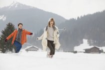 Happy couple running in snowy field — Stock Photo