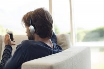 Man listening to headphones on sofa, rear view — Stock Photo