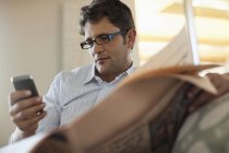 Mann benutzt Handy und liest Zeitung — Stockfoto