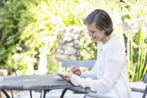 Женщина с цифровым планшетом за столом на открытом воздухе — стоковое фото