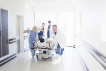 Doctors and nurses rushing patient on stretcher down hospital corridor — Stock Photo
