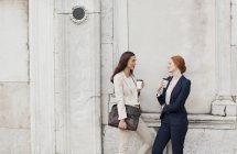 Mulheres de negócios sorridentes bebendo café e falando contra a parede da construção — Fotografia de Stock