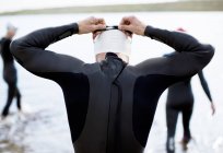 Triathlete adjusting goggles at start of race, rear view — Stock Photo