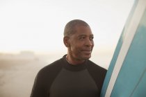 Surfeur plus âgé portant la planche sur la plage — Photo de stock