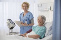 Ritratto di infermiera sorridente e paziente anziano in camera d'ospedale — Foto stock