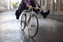 Geschnittenes Bild eines Geschäftsmannes, der mit den Füßen im Regen Fahrrad fährt — Stockfoto